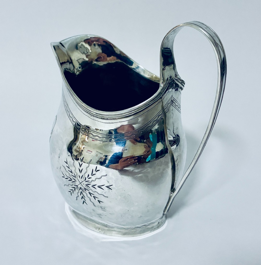 A Georgian sterling silver cream jug featuring a high loop handle, poured spout, and bright-cut star motif engraving on its body. View VI