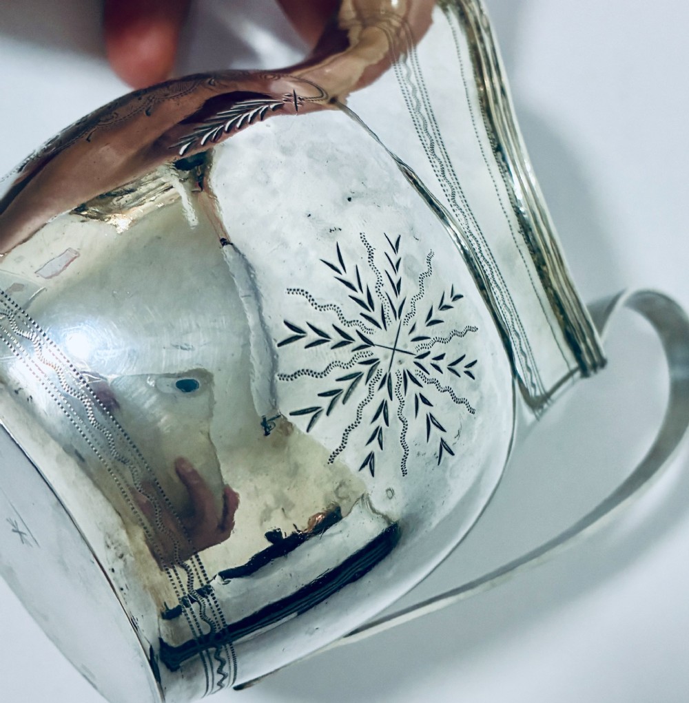 A Georgian sterling silver cream jug featuring a high loop handle, poured spout, and bright-cut star motif engraving on its body. View VII