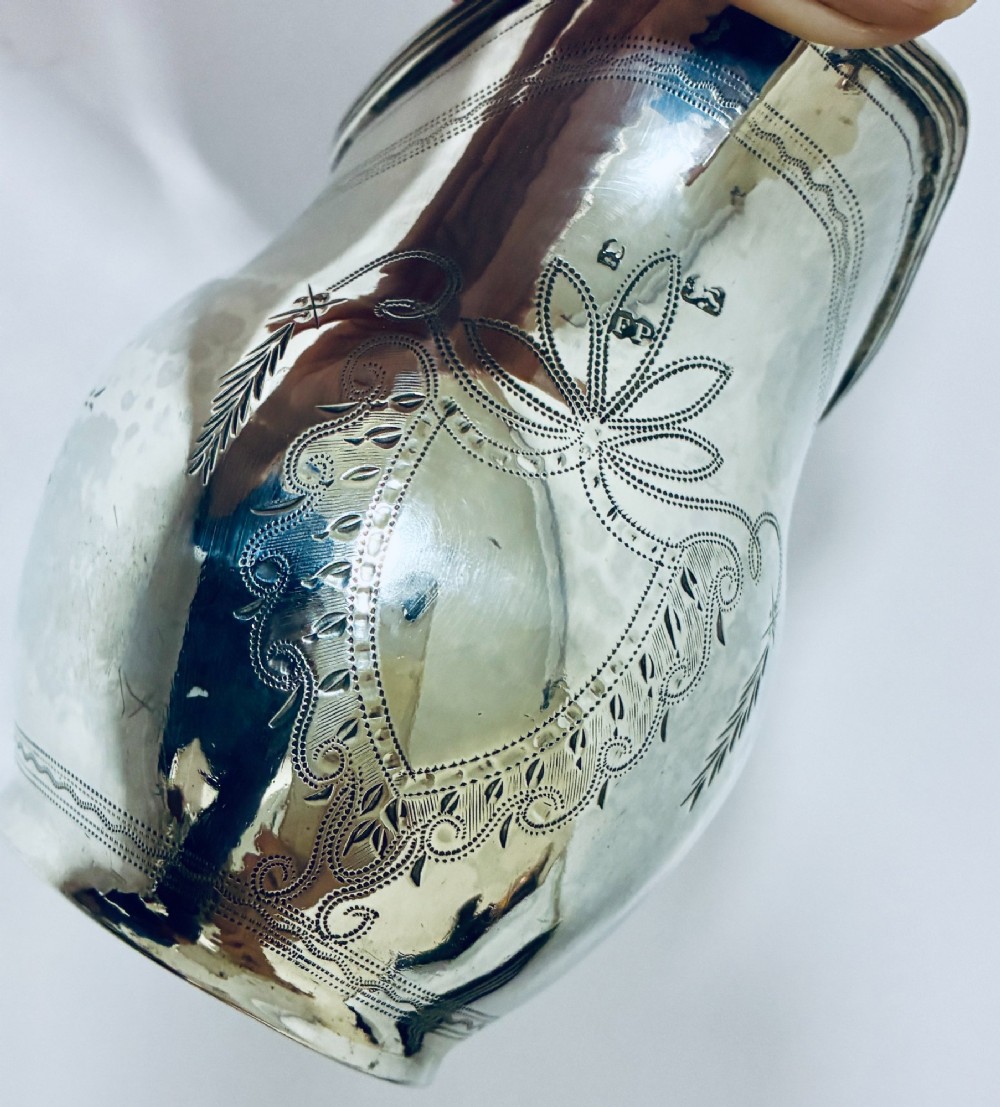 A Georgian sterling silver cream jug featuring a high loop handle, poured spout, and bright-cut star motif engraving on its body. View VIII