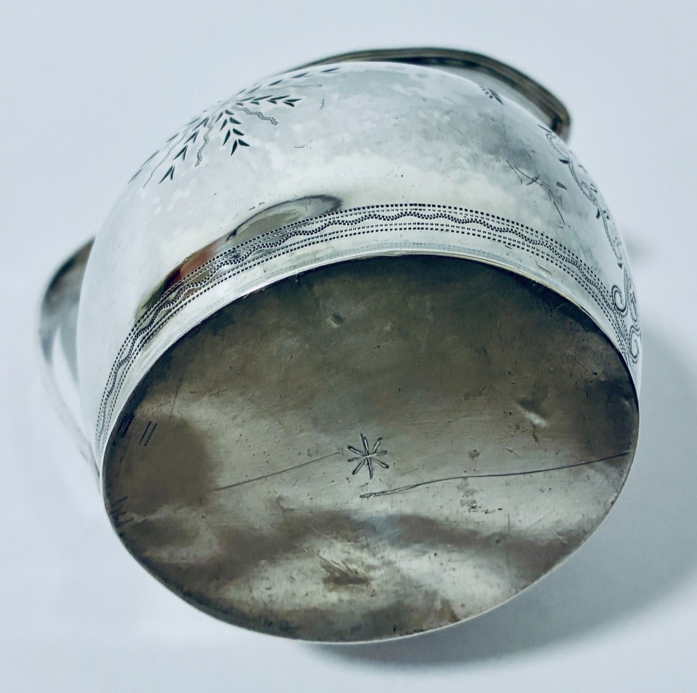 A Georgian sterling silver cream jug featuring a high loop handle, poured spout, and bright-cut star motif engraving on its body. View X