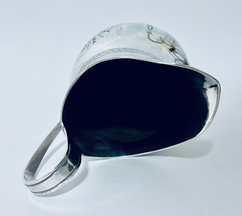 A Georgian sterling silver cream jug featuring a high loop handle, poured spout, and bright-cut star motif engraving on its body. View XI