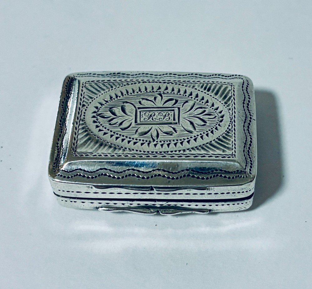 A small rectangular Georgian sterling silver vinaigrette box featuring bright-cut foliage engraving and a central monogrammed cartouche.