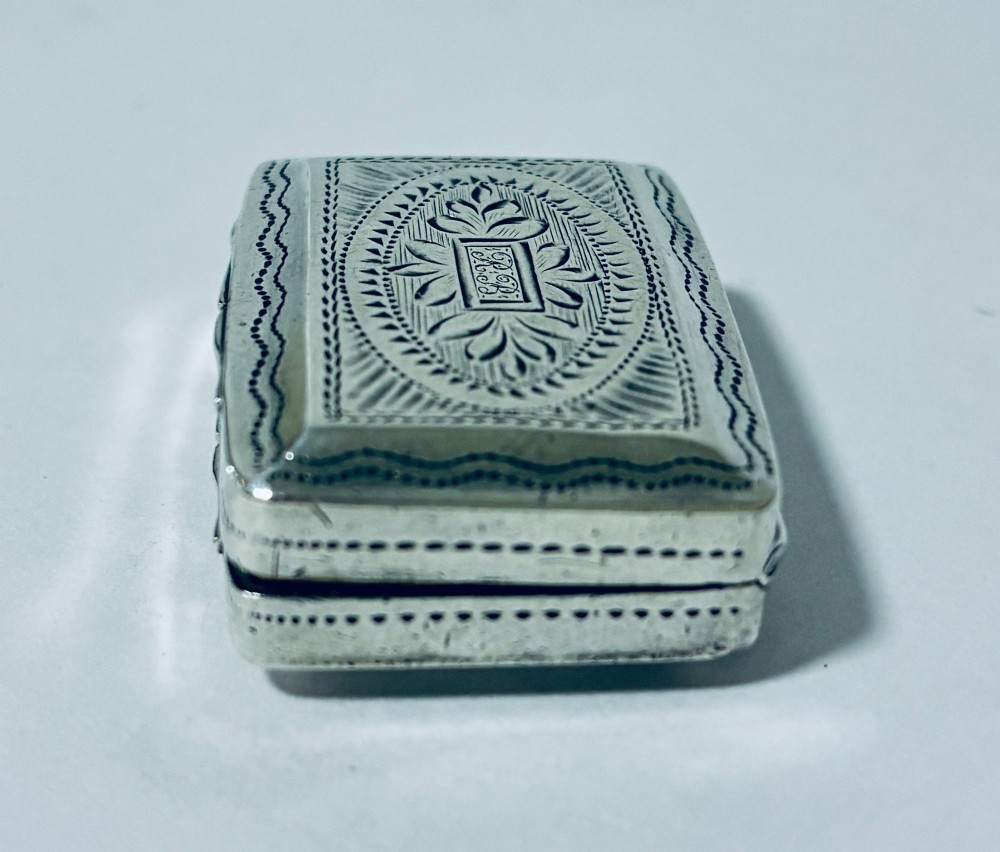 A small rectangular Georgian sterling silver vinaigrette box featuring bright-cut foliage engraving and a central monogrammed cartouche. View IV