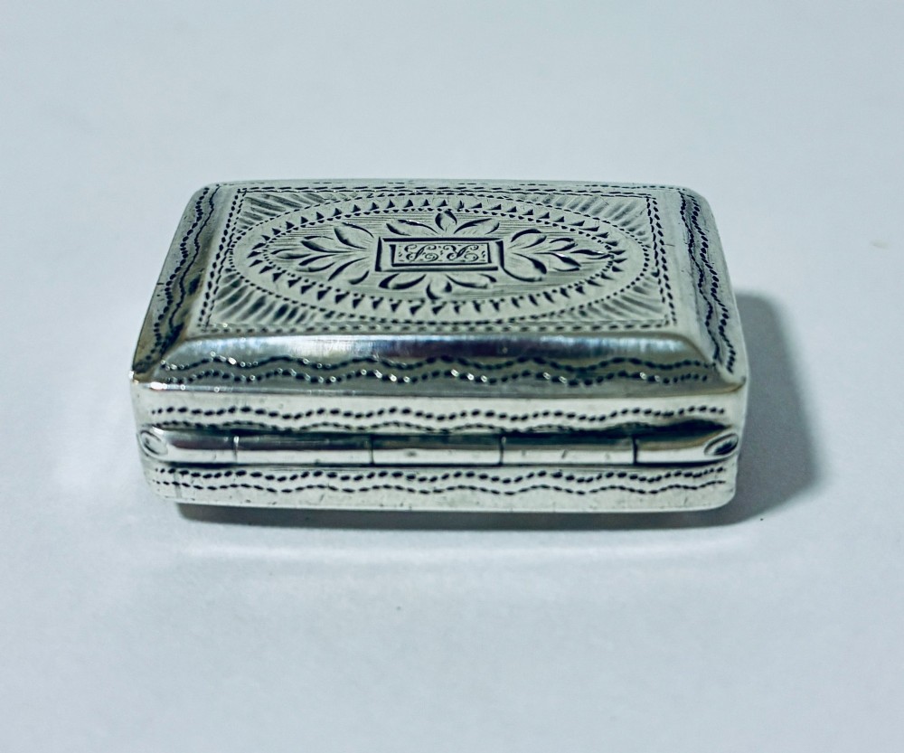 A small rectangular Georgian sterling silver vinaigrette box featuring bright-cut foliage engraving and a central monogrammed cartouche. View V