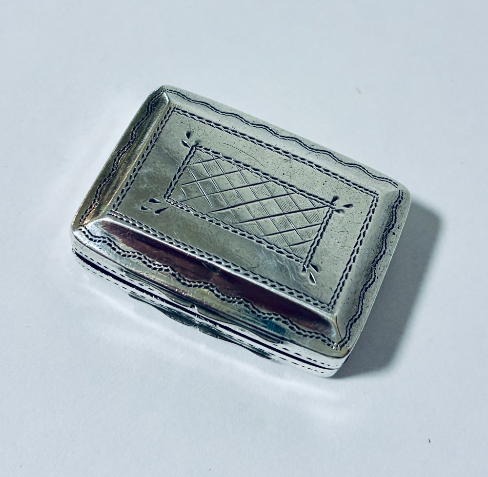 A small rectangular Georgian sterling silver vinaigrette box featuring bright-cut foliage engraving and a central monogrammed cartouche. View VII