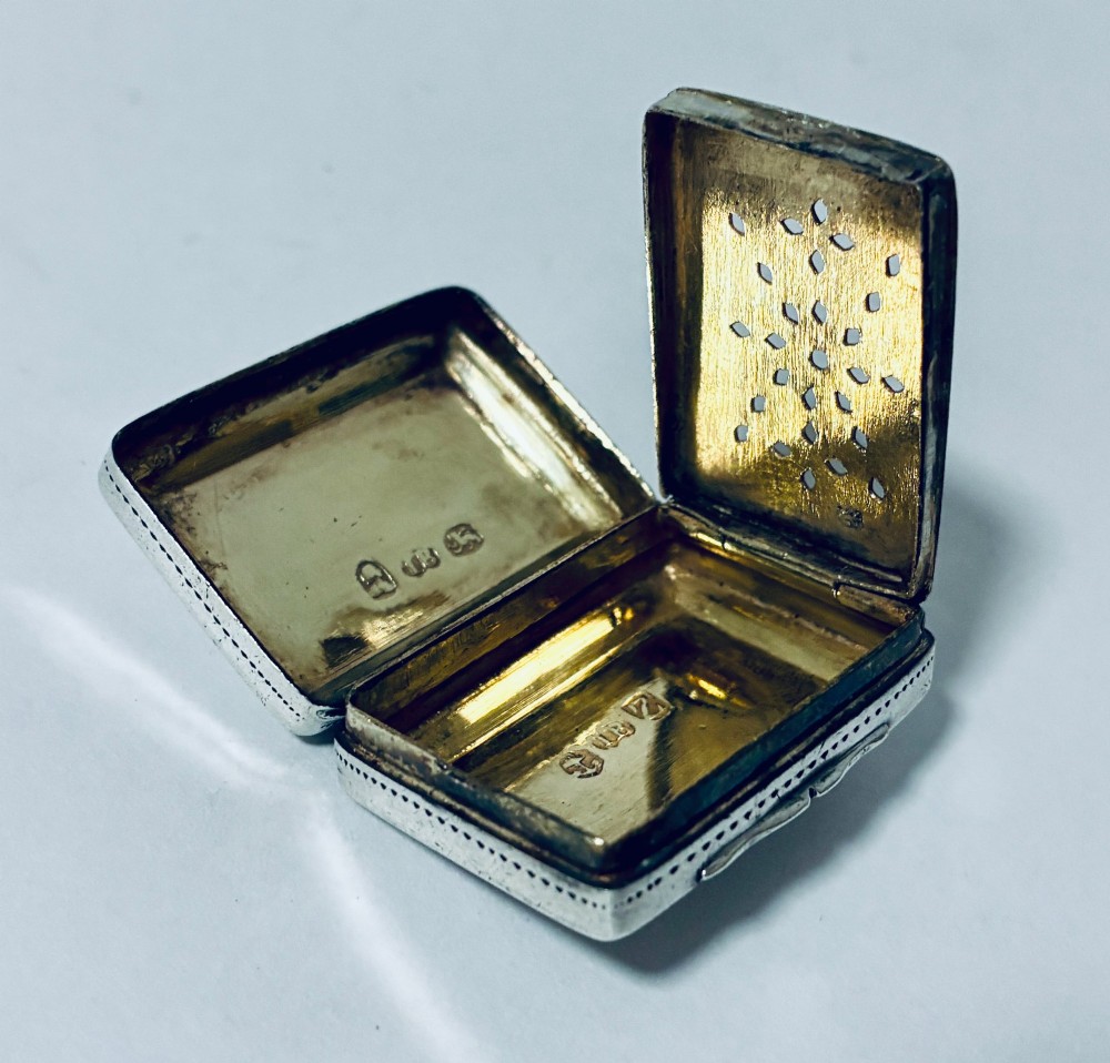 A small rectangular Georgian sterling silver vinaigrette box featuring bright-cut foliage engraving and a central monogrammed cartouche. View X
