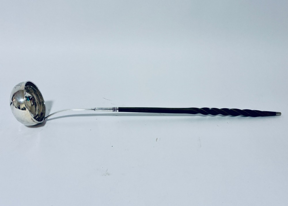 An antique Georgian silver toddy ladle featuring a deep circular silver bowl attached to a long, dark twisted handle.