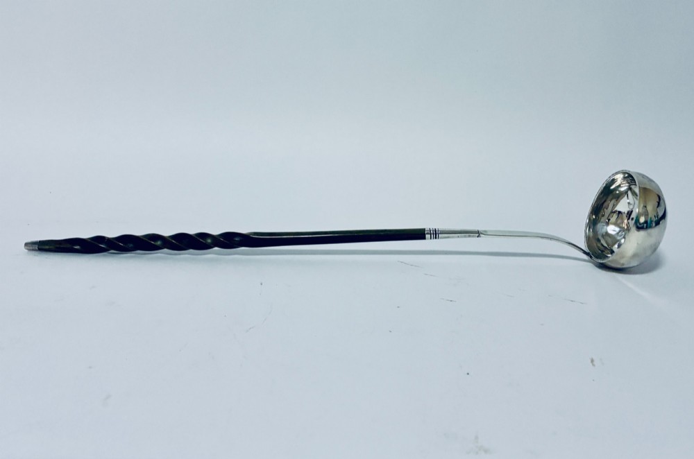 An antique Georgian silver toddy ladle featuring a deep circular silver bowl attached to a long, dark twisted handle. View IX