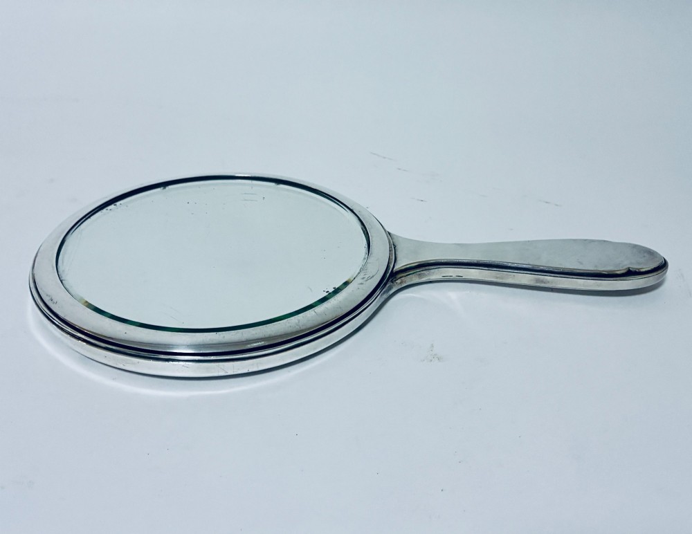 An antique oval silver hand mirror resting horizontally against a plain background.