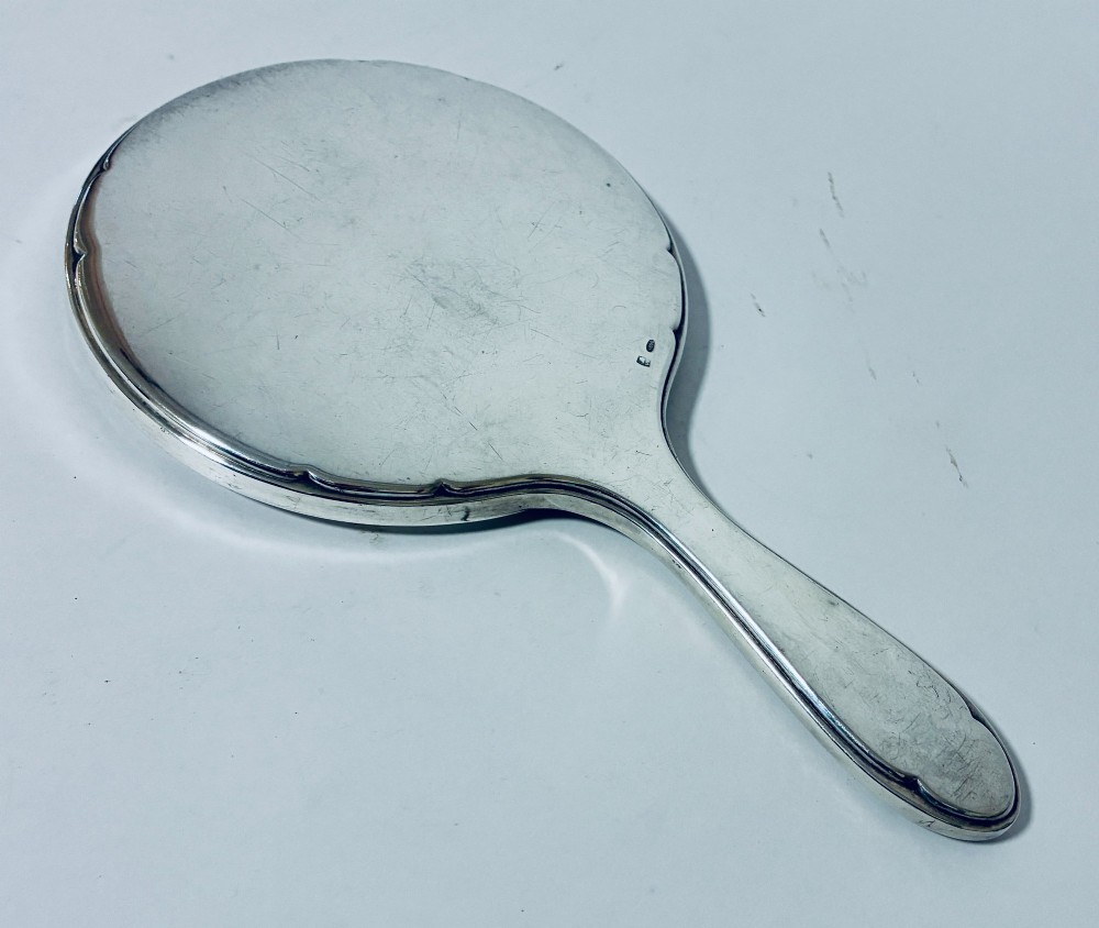 An antique oval silver hand mirror resting horizontally against a plain background. View VI