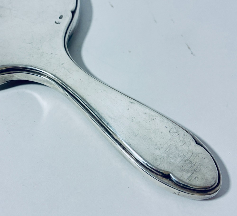 An antique oval silver hand mirror resting horizontally against a plain background. View VII