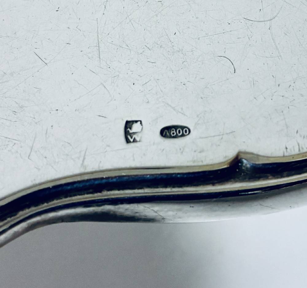 An antique oval silver hand mirror resting horizontally against a plain background. View VIII