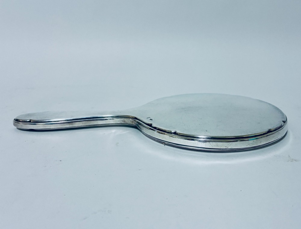 An antique oval silver hand mirror resting horizontally against a plain background. View IX