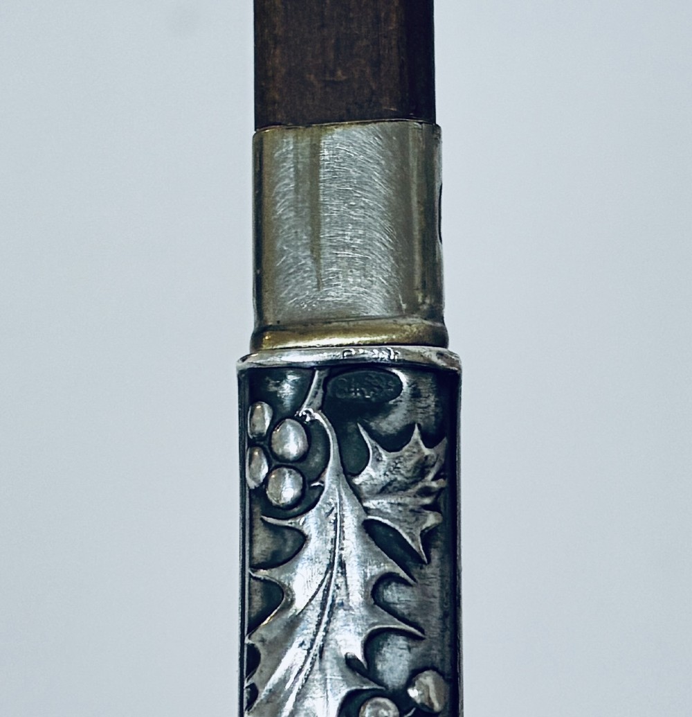 An antique silver cylindrical pencil holder featuring repousse holly leaf and berry decoration with a suspension ring attached to the end. View VI