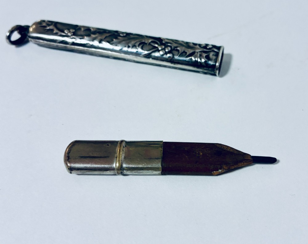 An antique silver cylindrical pencil holder featuring repousse holly leaf and berry decoration with a suspension ring attached to the end. View VII
