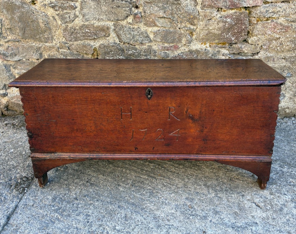 A long early 18th-century oak sword chest featuring a hinged lid, hand-carved initials H R, the date 1724 on the front panel, and a central iron escutcheon.