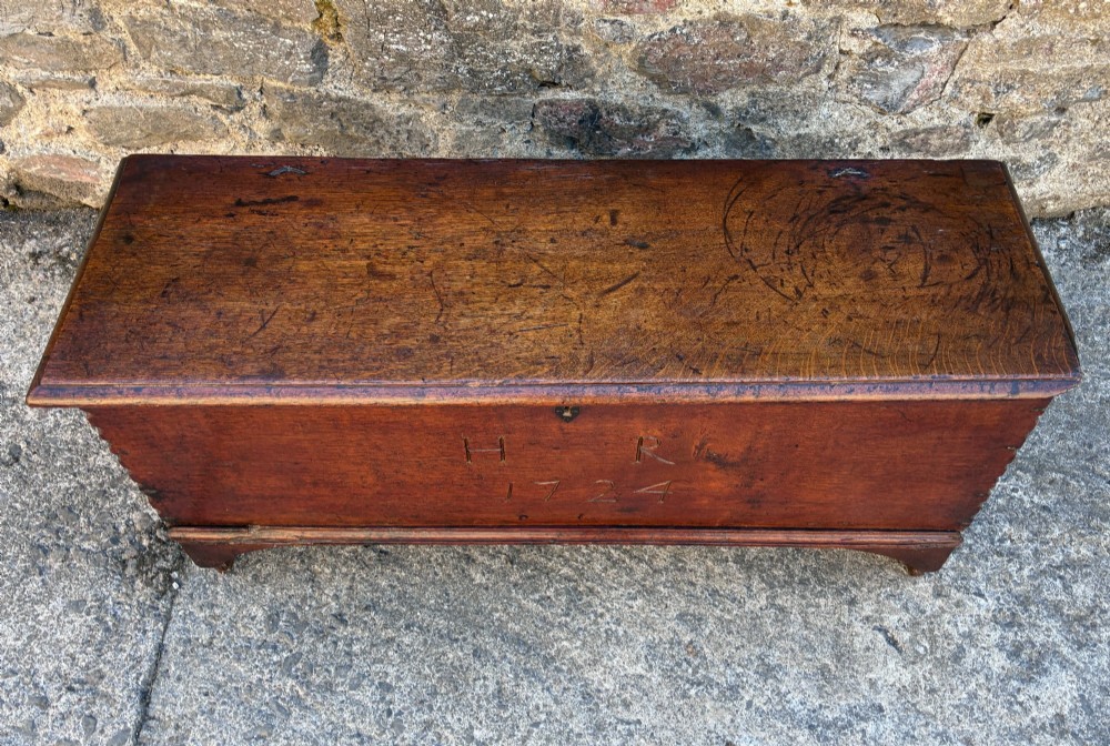 A long early 18th-century oak sword chest featuring a hinged lid, hand-carved initials H R, the date 1724 on the front panel, and a central iron escutcheon. View II