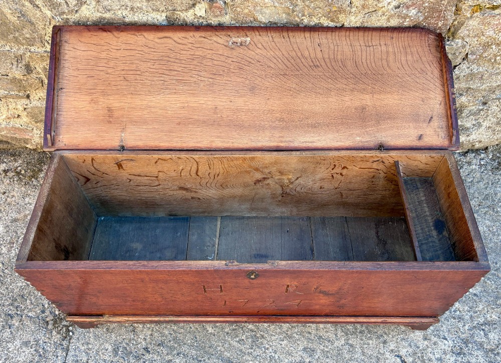 A long early 18th-century oak sword chest featuring a hinged lid, hand-carved initials H R, the date 1724 on the front panel, and a central iron escutcheon. View V