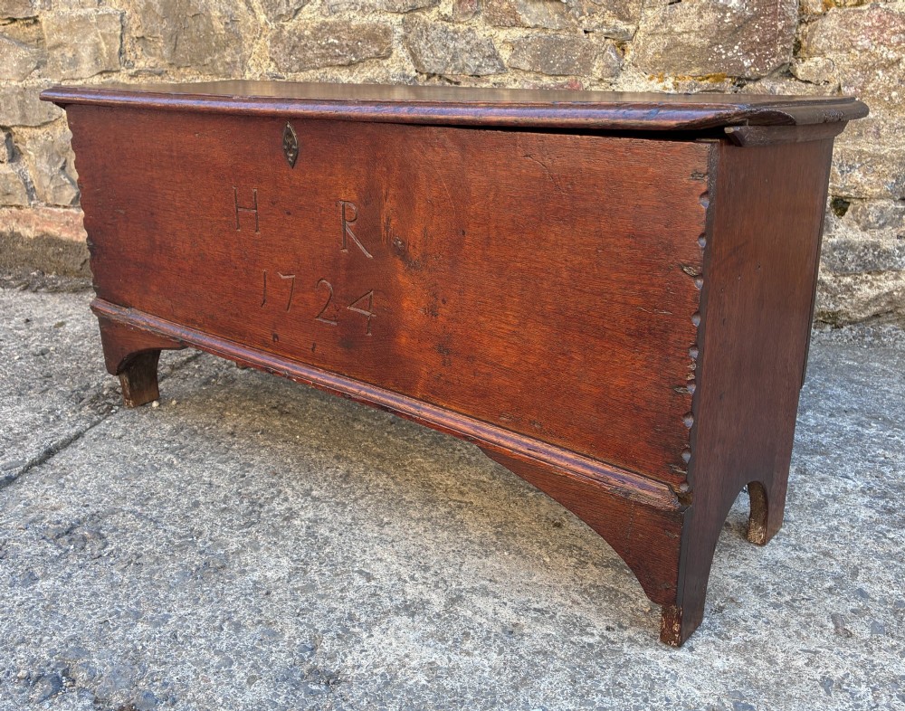 A long early 18th-century oak sword chest featuring a hinged lid, hand-carved initials H R, the date 1724 on the front panel, and a central iron escutcheon. View X