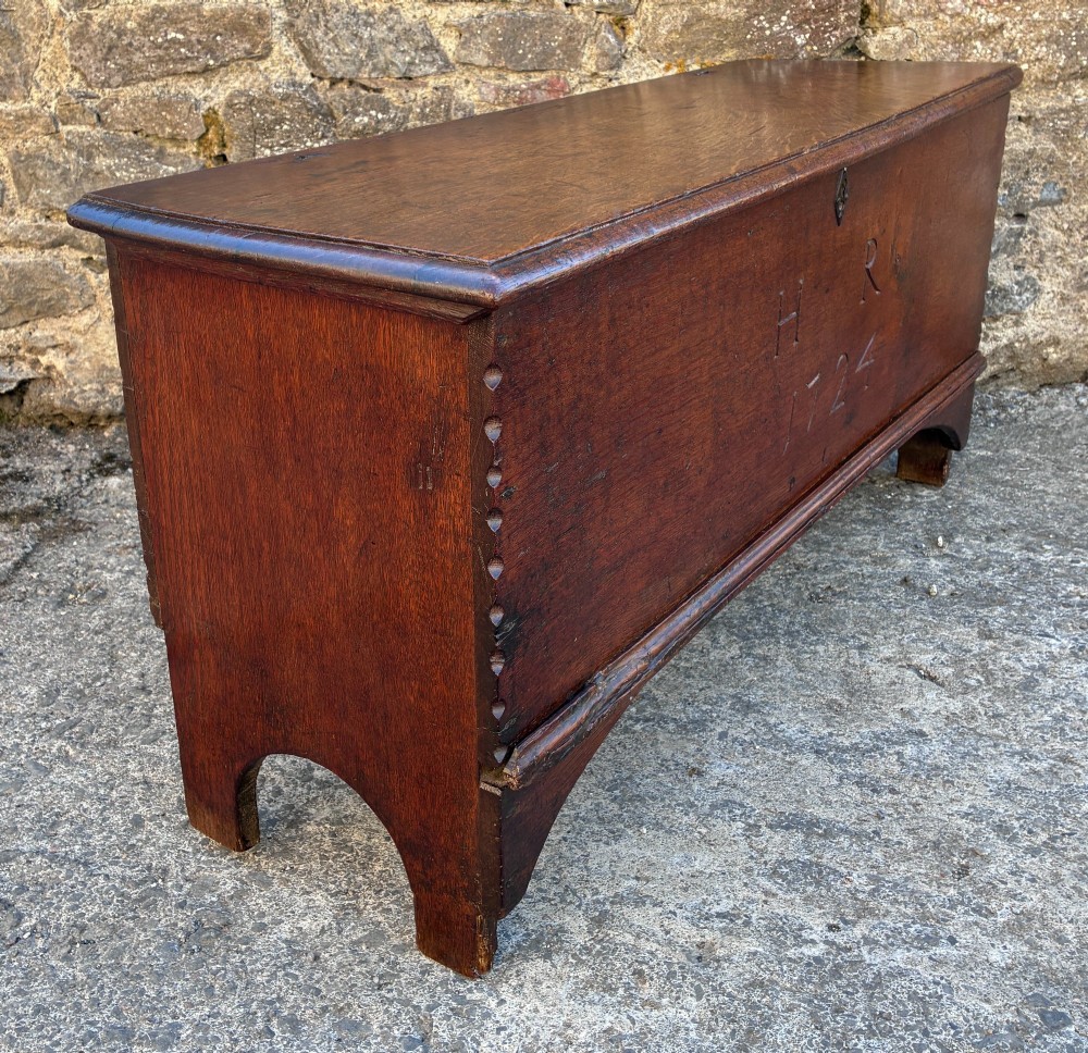 A long early 18th-century oak sword chest featuring a hinged lid, hand-carved initials H R, the date 1724 on the front panel, and a central iron escutcheon. View XIV