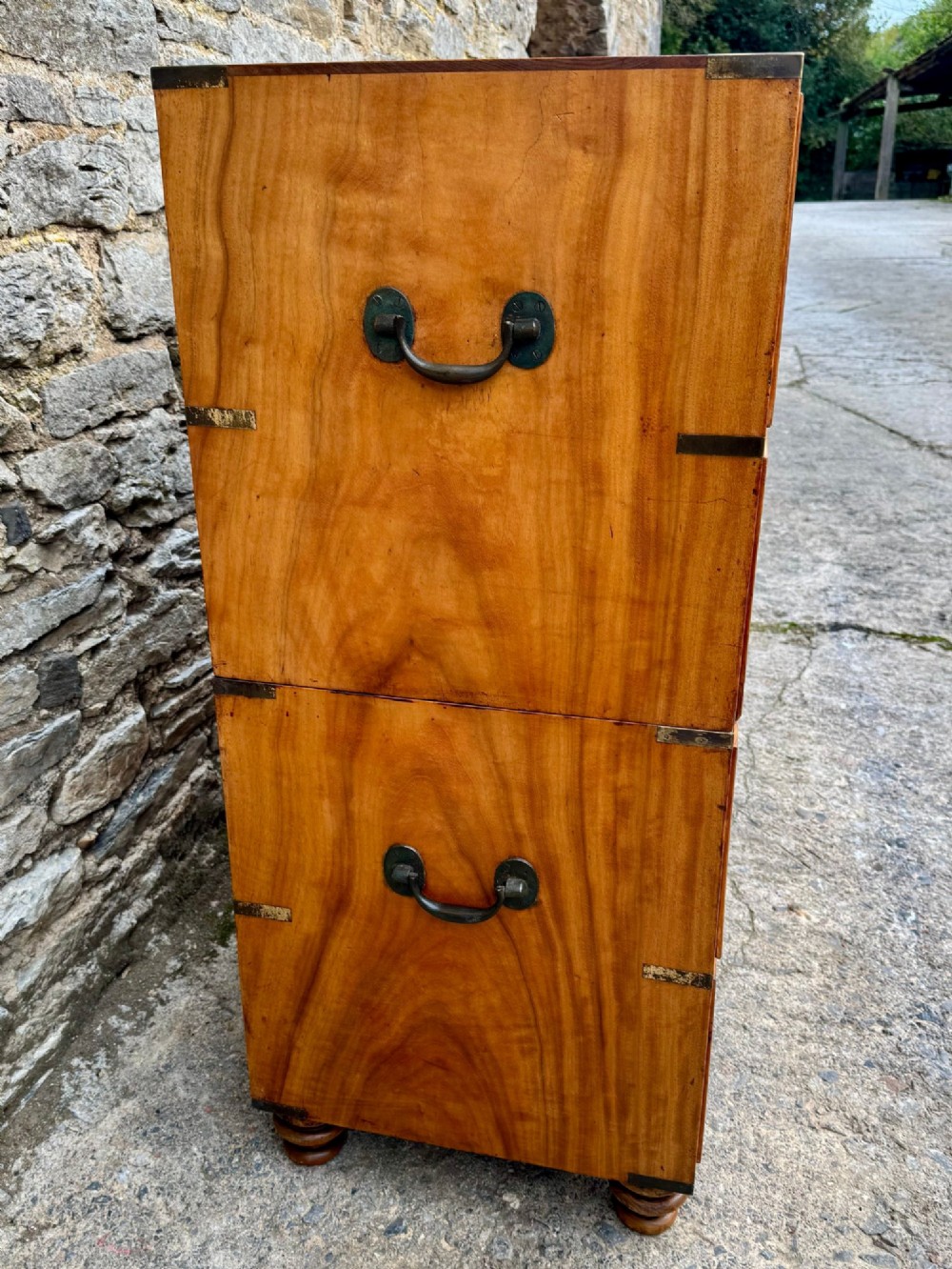 A Victorian camphor wood military campaign chest of drawers featuring two short over three long drawers with flush brass handles, corner straps, and turned feet. View II
