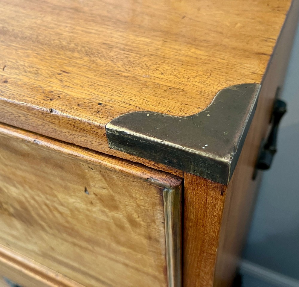 A Victorian camphor wood military campaign chest of drawers featuring two short over three long drawers with flush brass handles, corner straps, and turned feet. View V