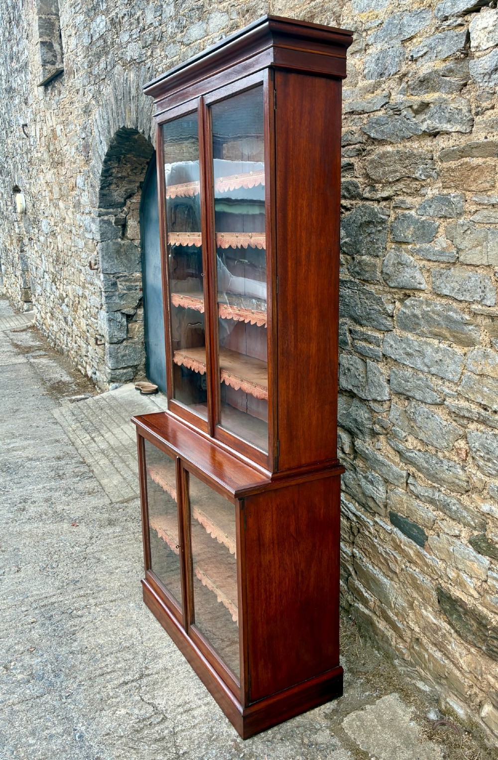 A tall Victorian mahogany cabinet featuring an upper two-door glazed section with scalloped shelf edging set above a lower matching glazed cupboard. View V