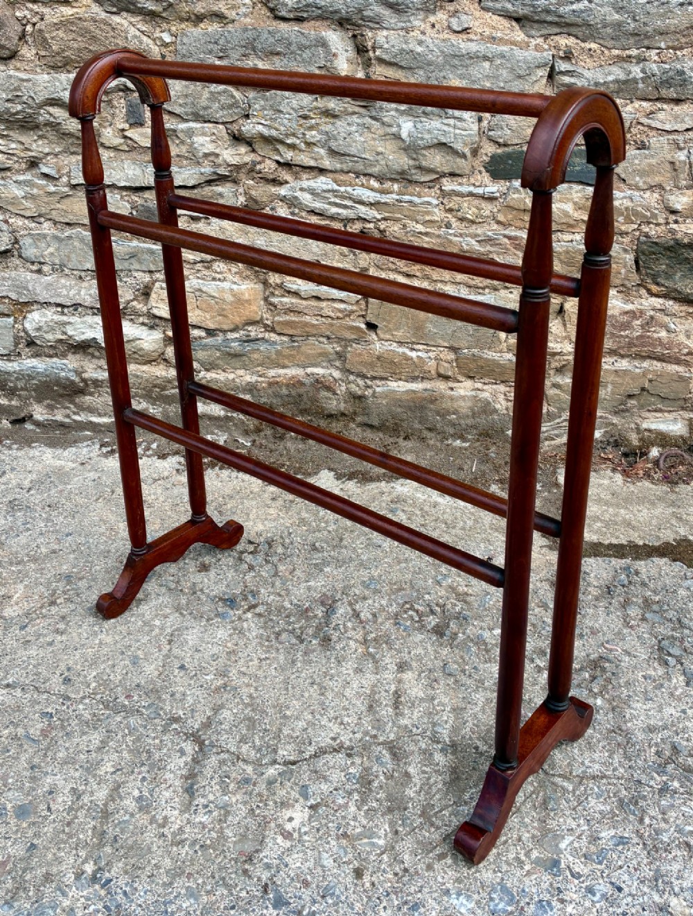 A freestanding Victorian mahogany towel rail featuring arched top cresting, turned upright supports, four horizontal bars, and shaped trestle feet.
