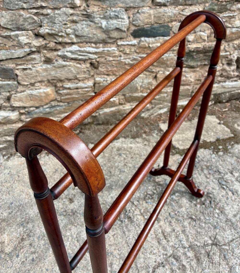 A freestanding Victorian mahogany towel rail featuring arched top cresting, turned upright supports, four horizontal bars, and shaped trestle feet. View V