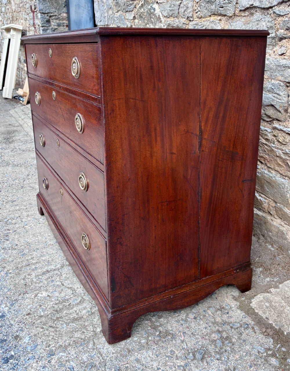 A Georgian mahogany chest of drawers featuring four graduated drawers with circular brass ring pull handles and bracket feet. View IV