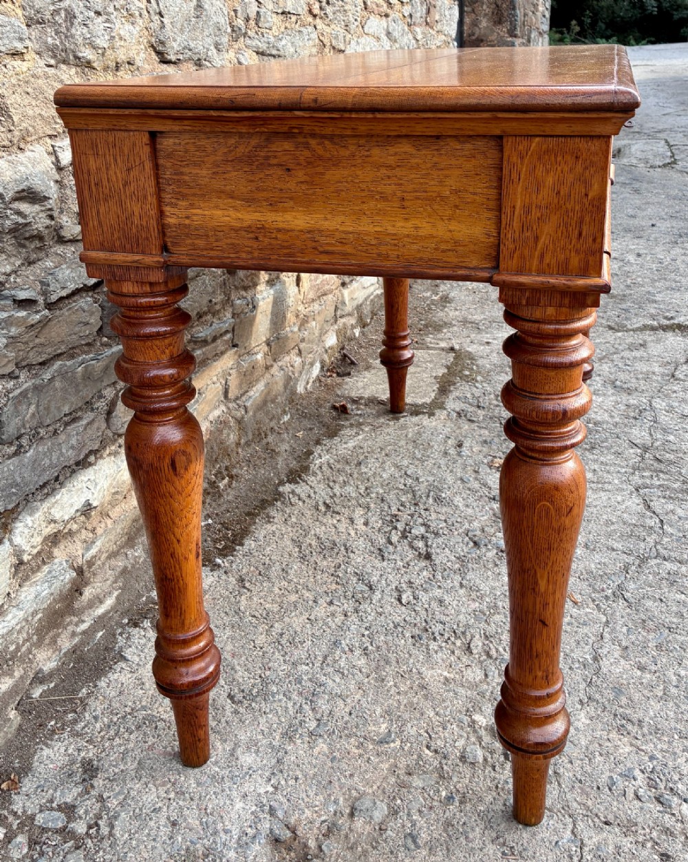 A Victorian golden oak console table featuring a rectangular top with a moulded edge, two frieze drawers, and four turned legs. View IV