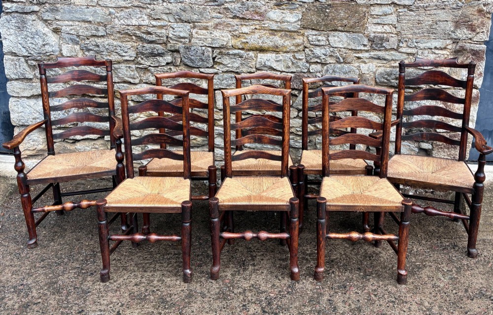 A set of eight 19th-century dark timber Lancashire ladderback dining chairs featuring wavy back slats, turned front stretchers, and woven rush seats, comprising two carver armchairs and six side chairs.