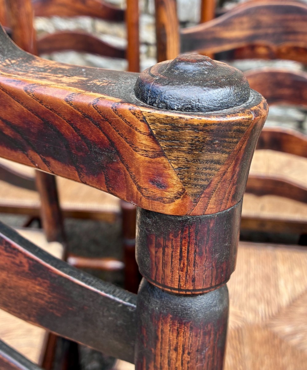 A set of eight 19th-century dark timber Lancashire ladderback dining chairs featuring wavy back slats, turned front stretchers, and woven rush seats, comprising two carver armchairs and six side chairs. View IV