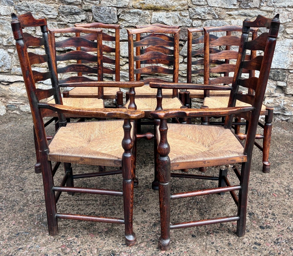 A set of eight 19th-century dark timber Lancashire ladderback dining chairs featuring wavy back slats, turned front stretchers, and woven rush seats, comprising two carver armchairs and six side chairs. View V