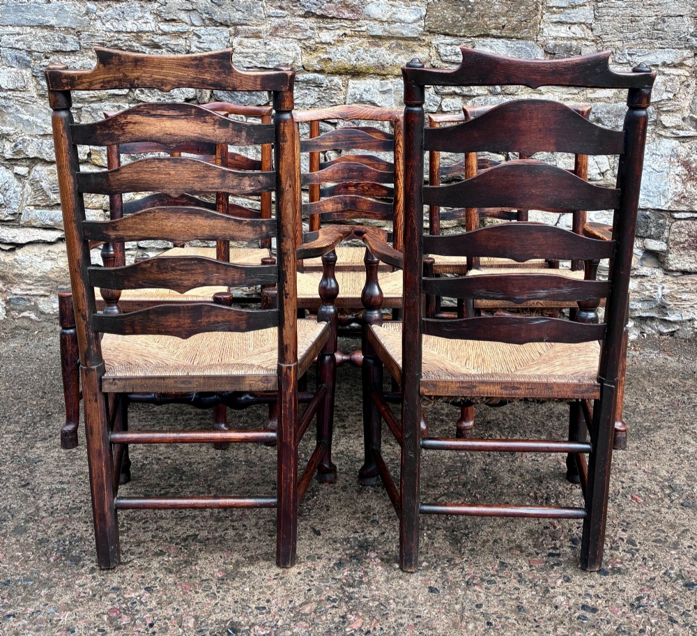A set of eight 19th-century dark timber Lancashire ladderback dining chairs featuring wavy back slats, turned front stretchers, and woven rush seats, comprising two carver armchairs and six side chairs. View VI