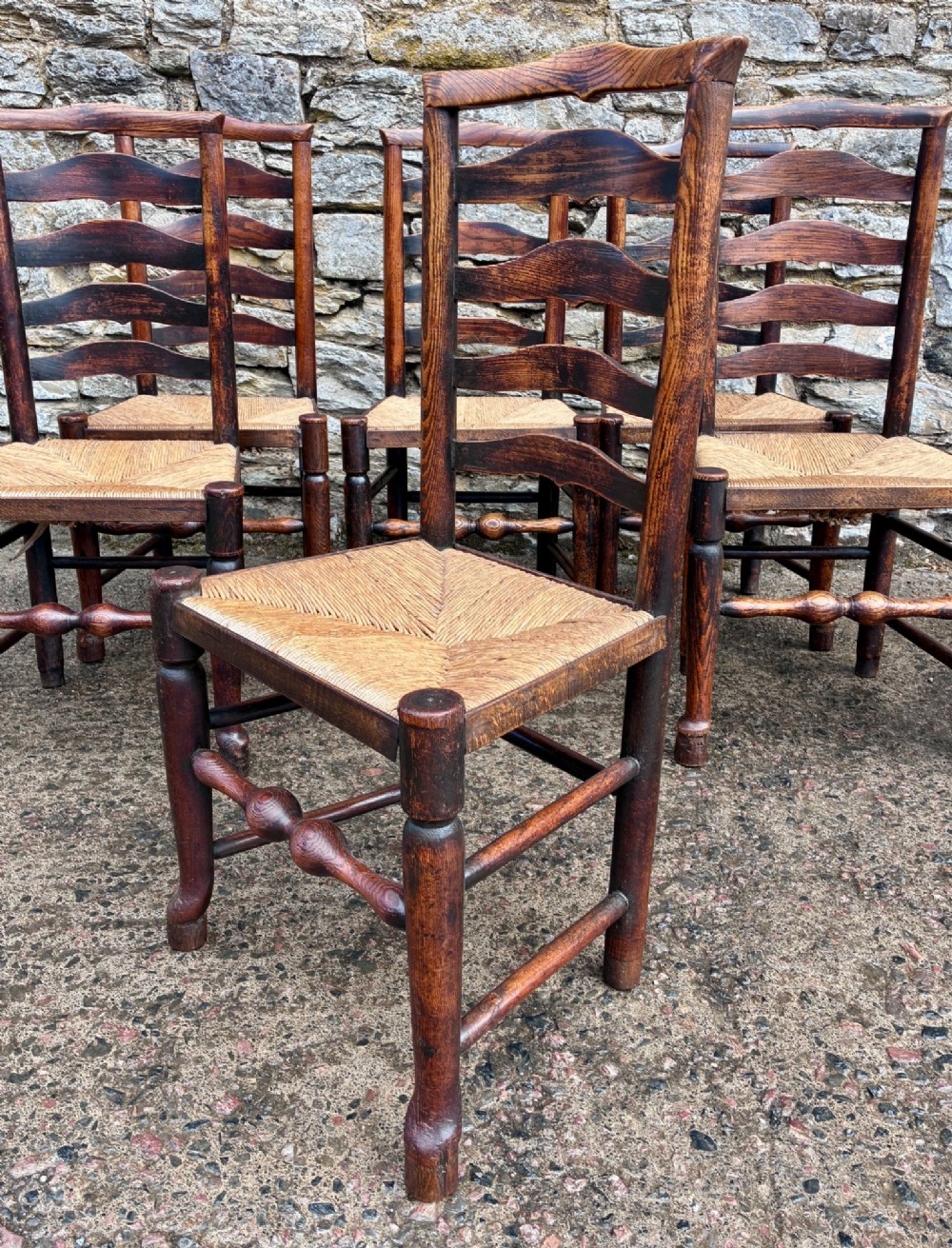 A set of eight 19th-century dark timber Lancashire ladderback dining chairs featuring wavy back slats, turned front stretchers, and woven rush seats, comprising two carver armchairs and six side chairs. View IX