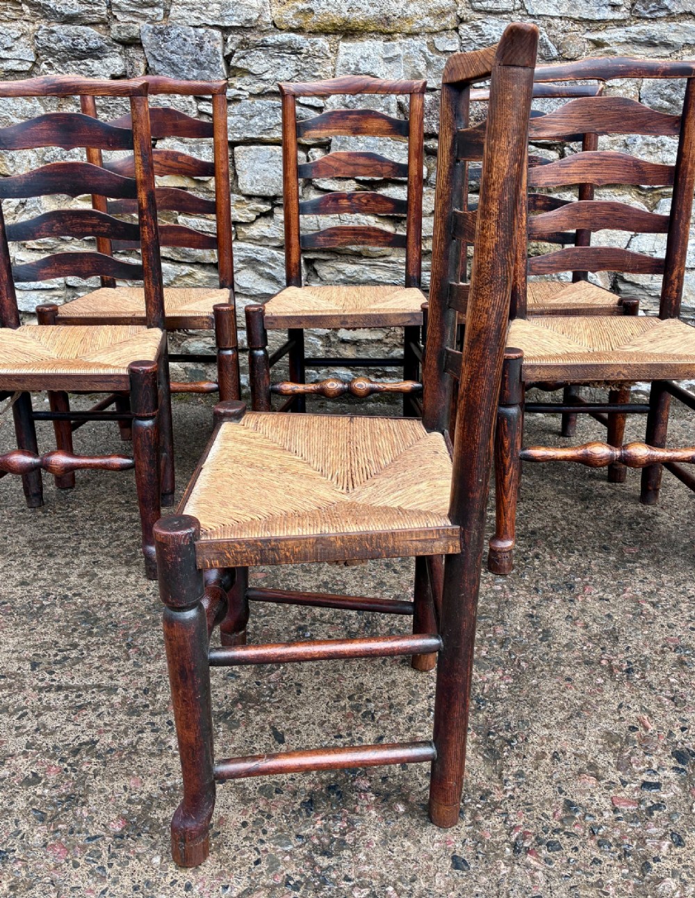 A set of eight 19th-century dark timber Lancashire ladderback dining chairs featuring wavy back slats, turned front stretchers, and woven rush seats, comprising two carver armchairs and six side chairs. View X