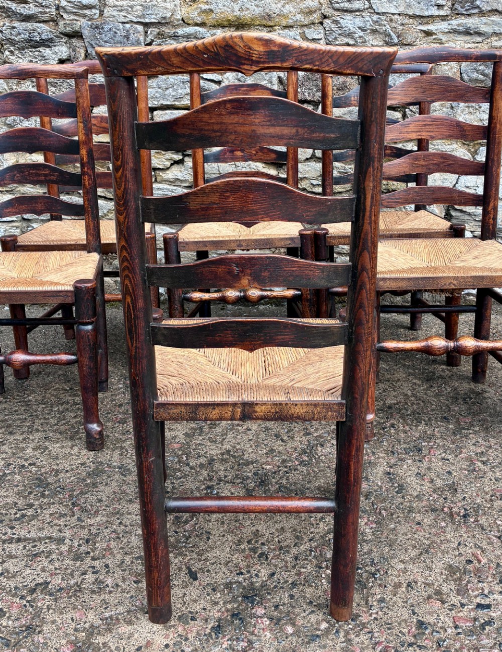 A set of eight 19th-century dark timber Lancashire ladderback dining chairs featuring wavy back slats, turned front stretchers, and woven rush seats, comprising two carver armchairs and six side chairs. View XI