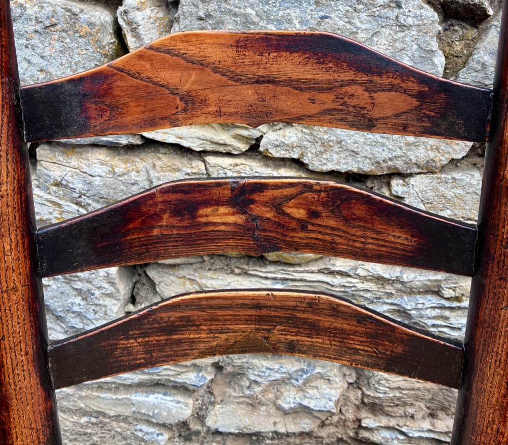A set of eight 19th-century dark timber Lancashire ladderback dining chairs featuring wavy back slats, turned front stretchers, and woven rush seats, comprising two carver armchairs and six side chairs. View XV