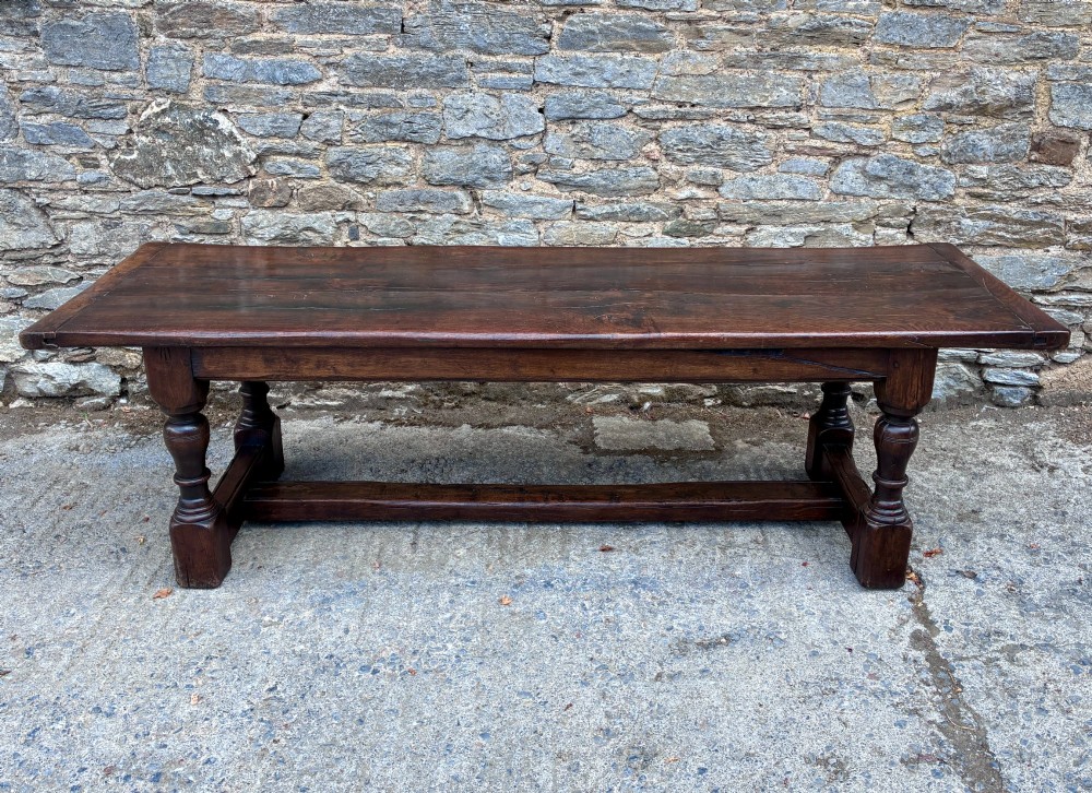 A long dark oak refectory dining table featuring a solid plank top, cleated ends, turned legs, and a low stretcher rail.