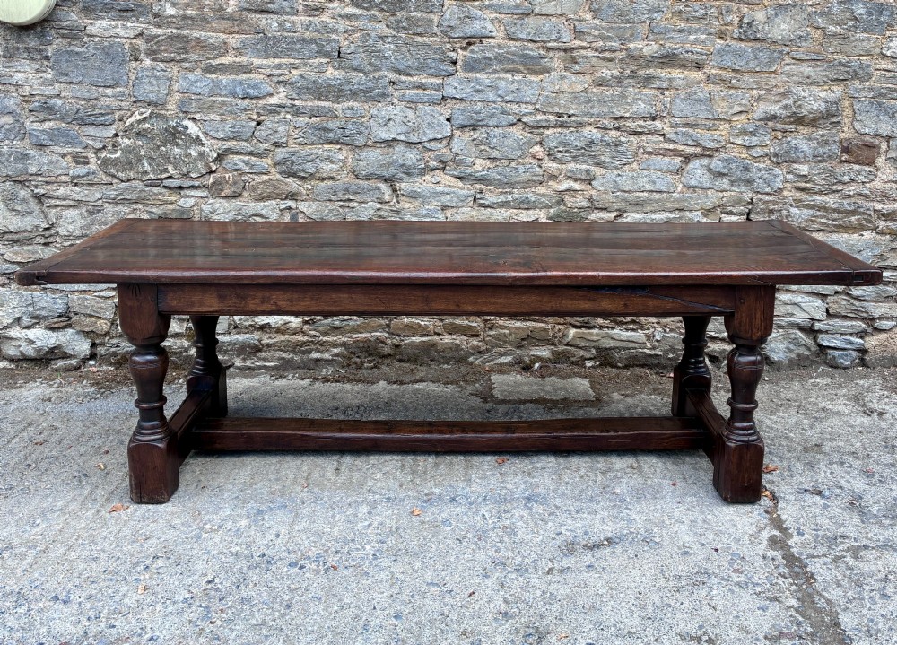 A long dark oak refectory dining table featuring a solid plank top, cleated ends, turned legs, and a low stretcher rail. View II