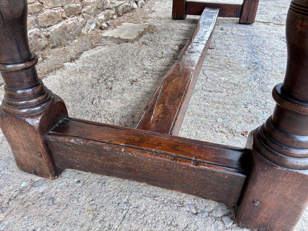 A long dark oak refectory dining table featuring a solid plank top, cleated ends, turned legs, and a low stretcher rail. View VIII