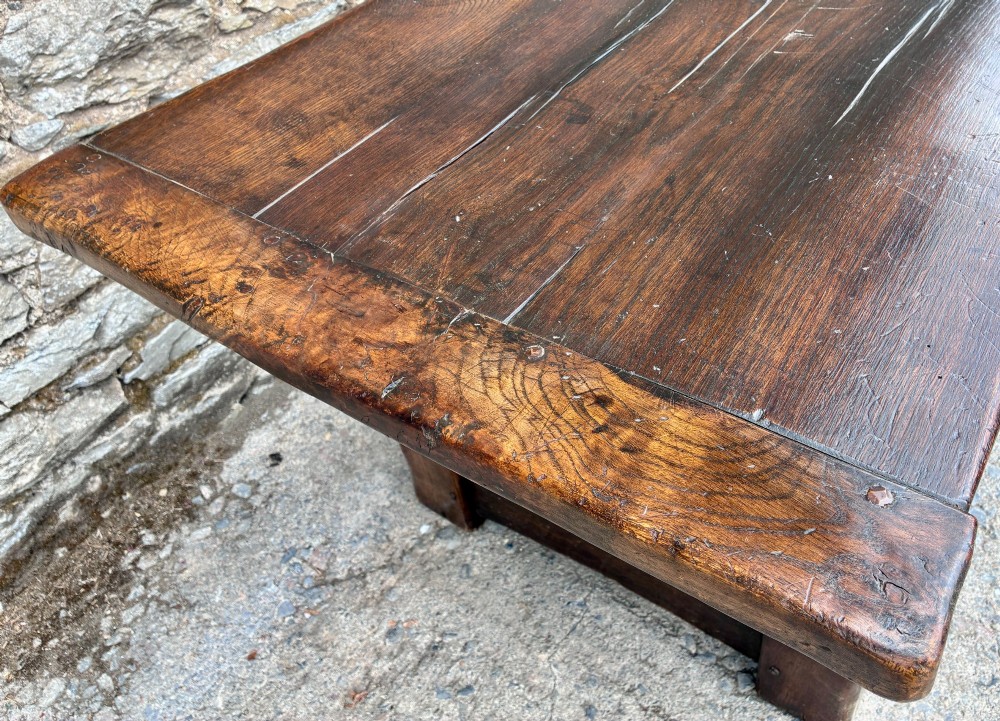 A long dark oak refectory dining table featuring a solid plank top, cleated ends, turned legs, and a low stretcher rail. View XI