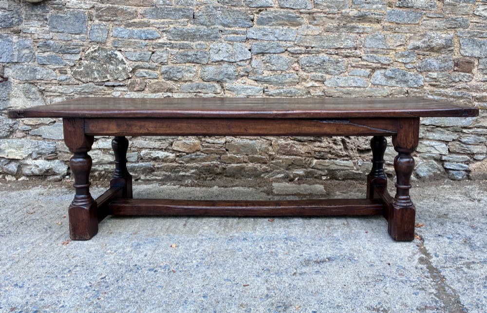 A long dark oak refectory dining table featuring a solid plank top, cleated ends, turned legs, and a low stretcher rail. View XIII