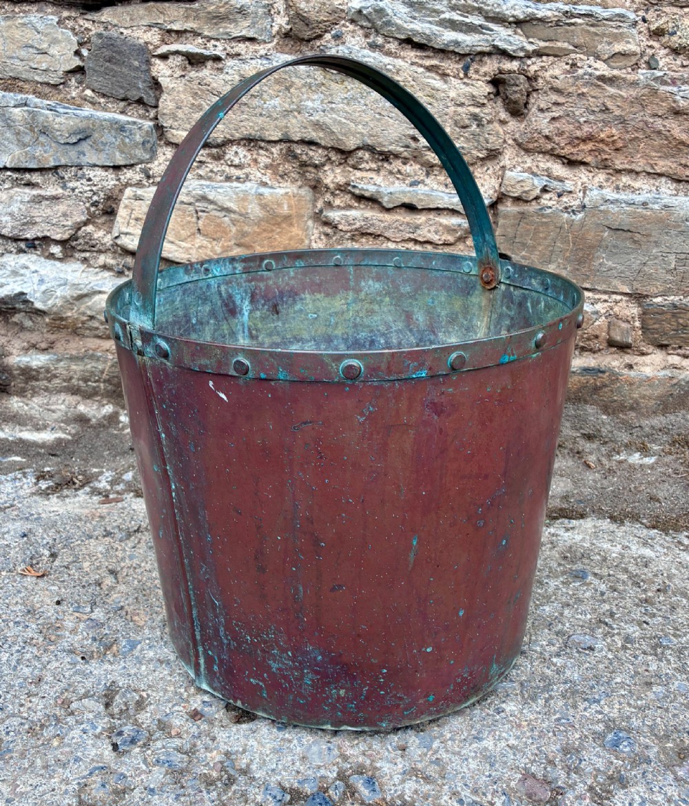 A cylindrical copper bucket featuring a riveted top band, a swing metal handle, and visible green verdigris patination. View III
