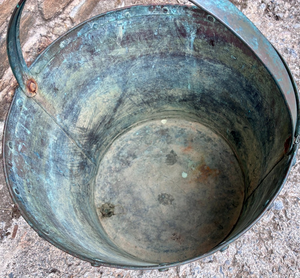 A cylindrical copper bucket featuring a riveted top band, a swing metal handle, and visible green verdigris patination. View VII