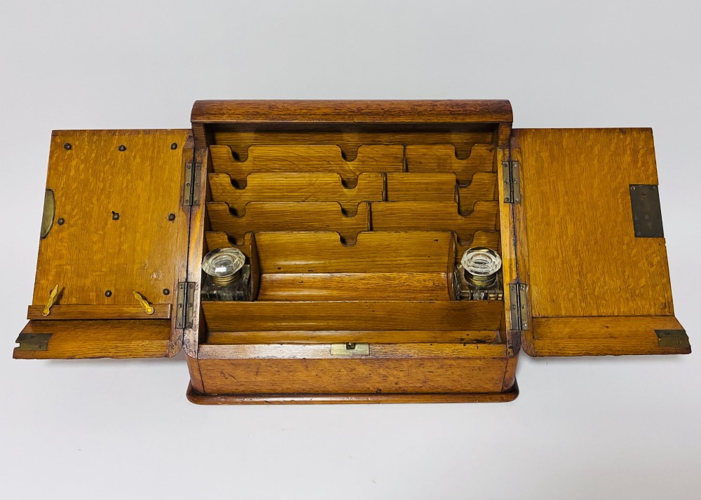 A Victorian oak stationery cabinet featuring sloped double doors, a metal escutcheon with a key, and a moulded plinth base. View II