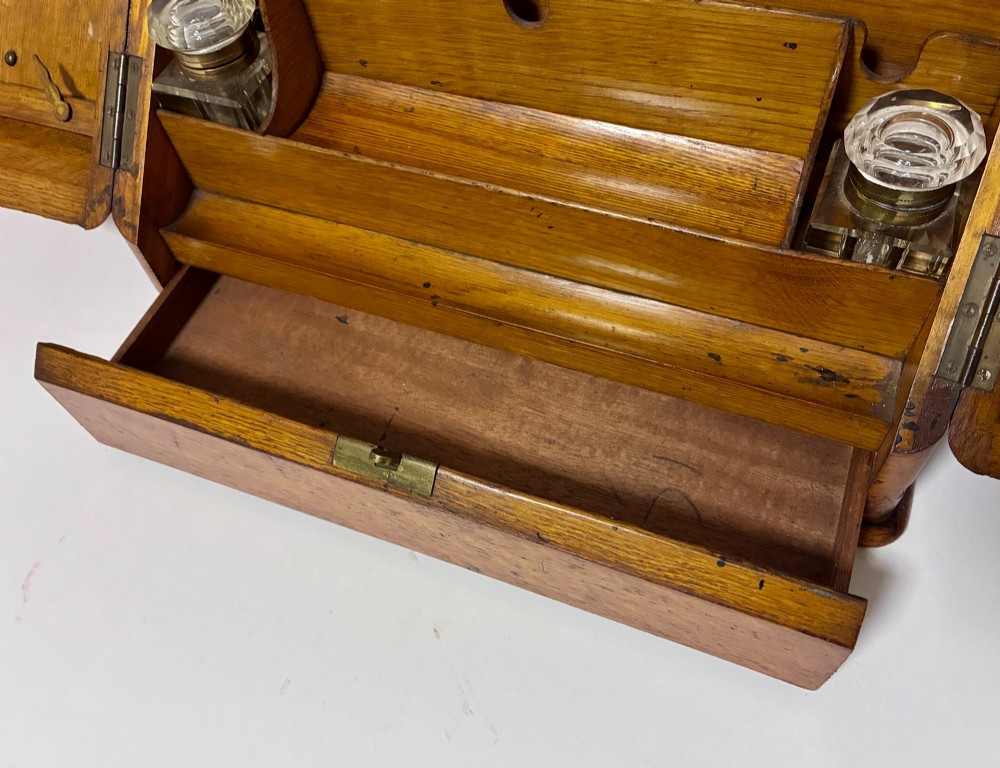 A Victorian oak stationery cabinet featuring sloped double doors, a metal escutcheon with a key, and a moulded plinth base. View IV