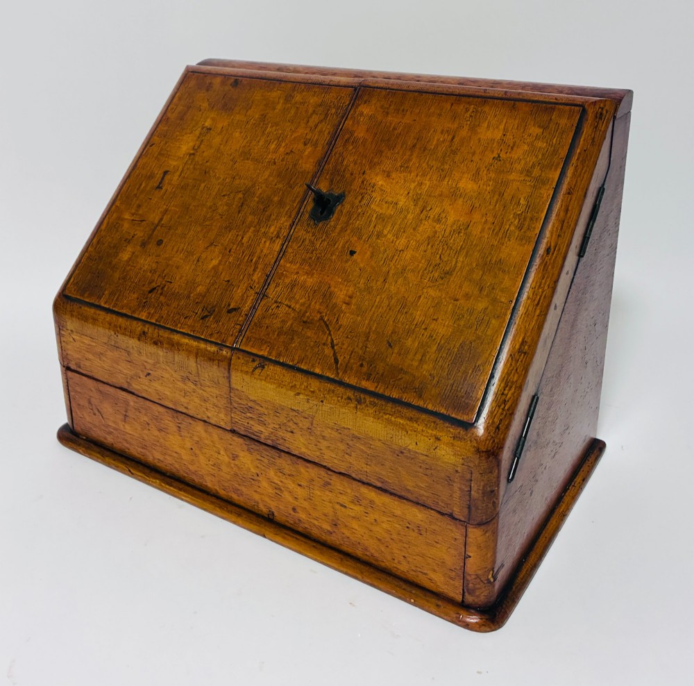 A Victorian oak stationery cabinet featuring sloped double doors, a metal escutcheon with a key, and a moulded plinth base. View VIII