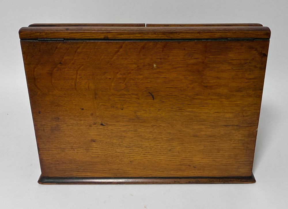 A Victorian oak stationery cabinet featuring sloped double doors, a metal escutcheon with a key, and a moulded plinth base. View X